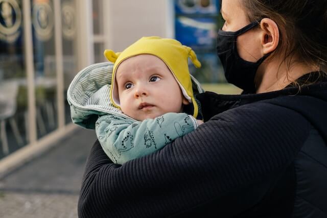 黄色い帽子をかぶった赤ちゃんがお母さんに抱っこされている